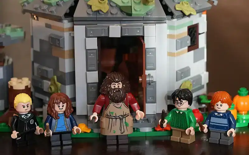 Lego-figuren van personages uit Harry Potter staan voor een gedetailleerd Lego-model van een huisje.