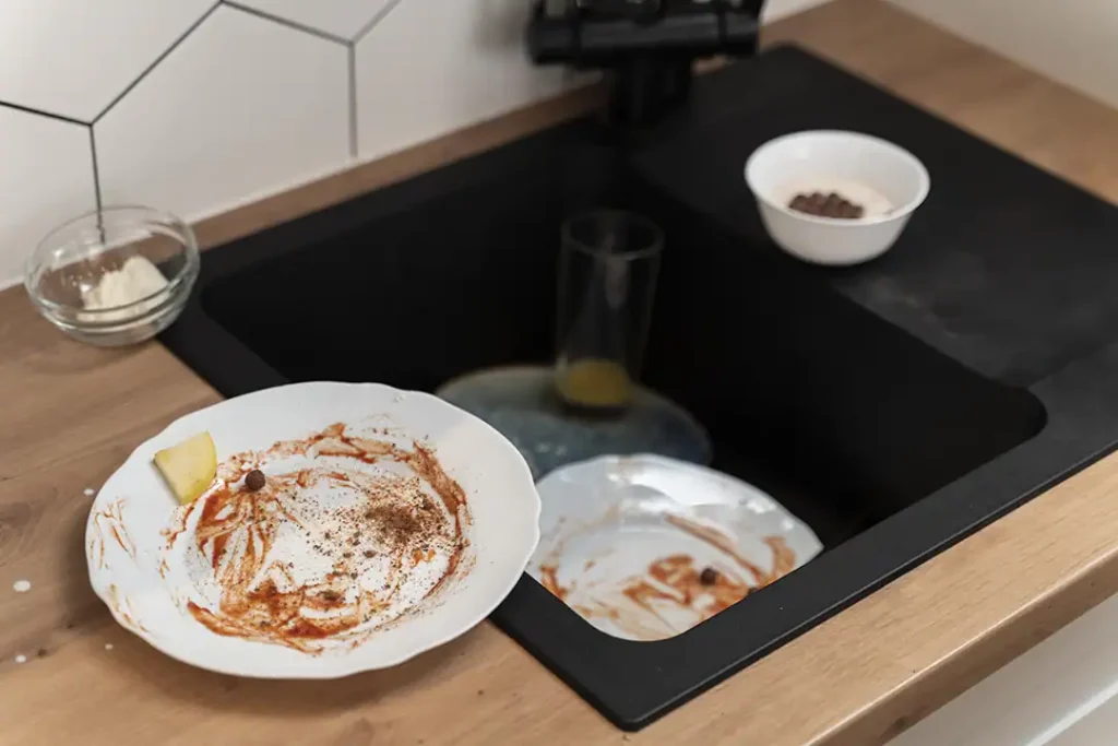 Dirty plates and food scraps in a sink that threatens to clog.