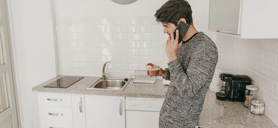 Man in a kitchen calling a plumber because the sink is clogged.