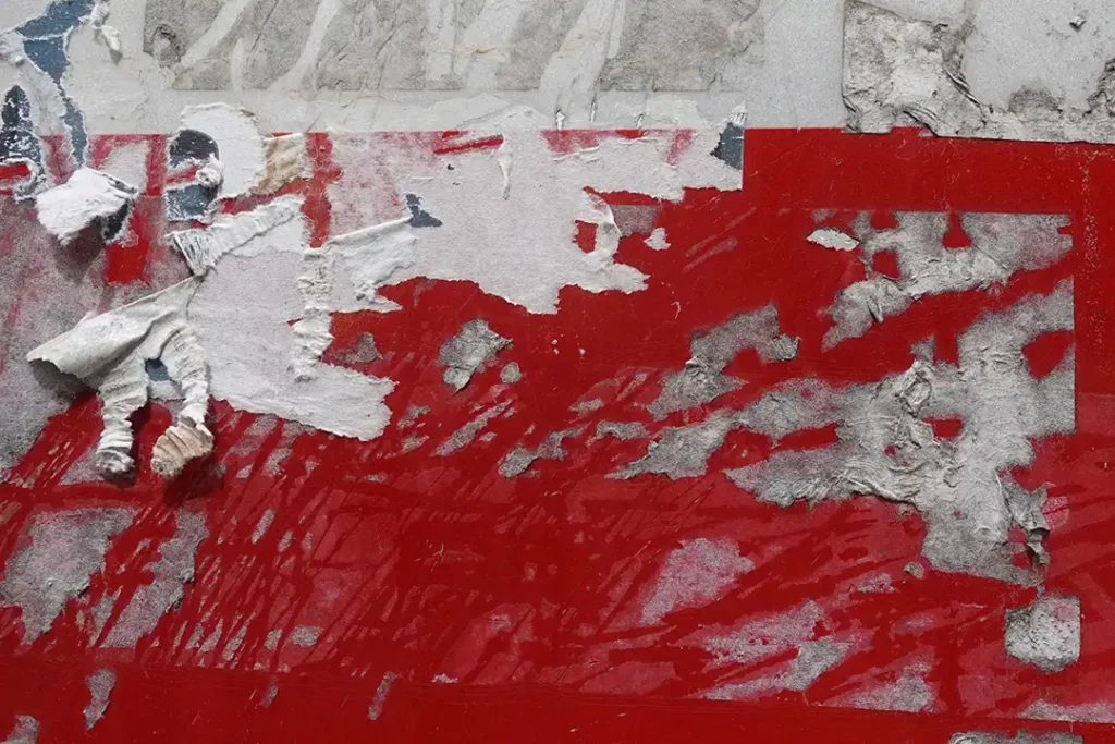 A close-up image of stubborn adhesive residue on a red surface, with partially torn and faded layers of paper and glue.