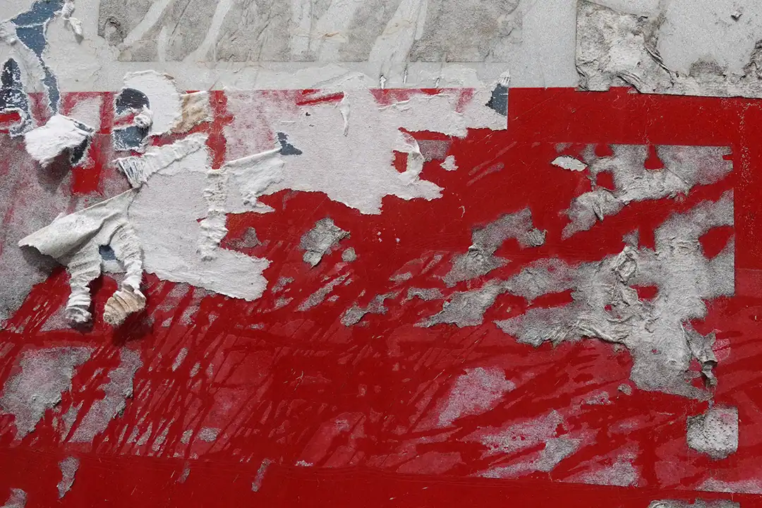 A close-up image of stubborn adhesive residue on a red surface, with partially torn and faded layers of paper and glue.
