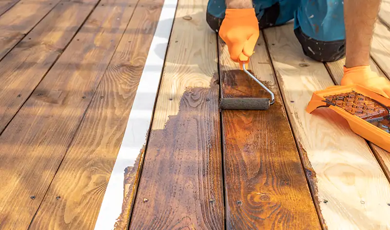Person treating a wooden deck with linseed oil using a paint roller.