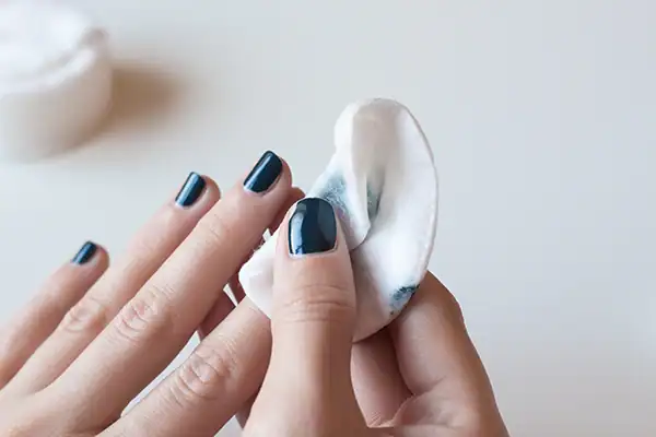 A person uses nail polish remover to carefully remove polish from a neat manicure.