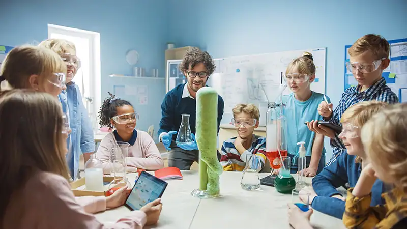 Children wearing safety goggles watch a classroom demonstration of the elephant toothpaste experiment.