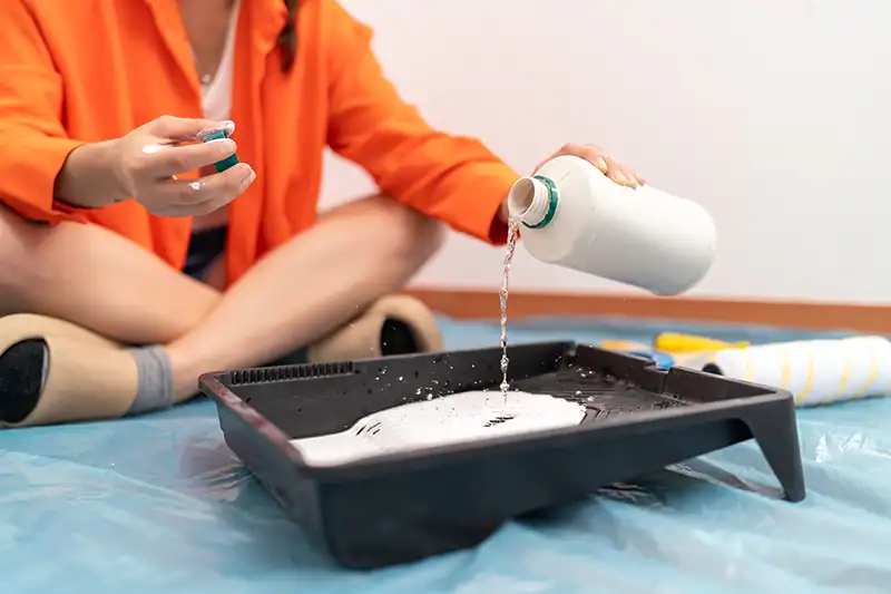 A person adding liquid to paint in a paint tray to thin the paint.