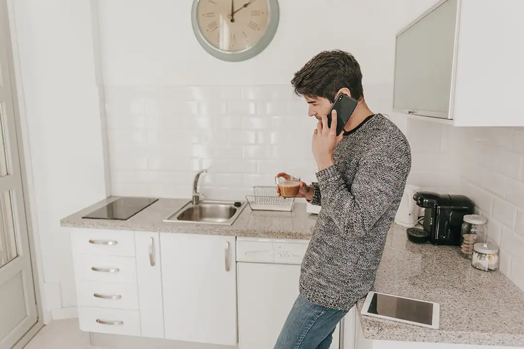 Man in a kitchen calling a plumber because the sink is clogged.