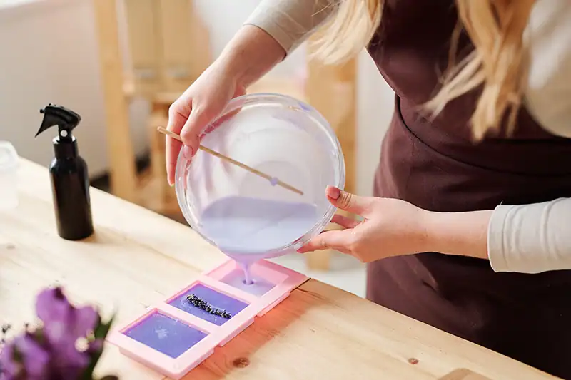 A person pours purple soap mixture into silicone soap molds.